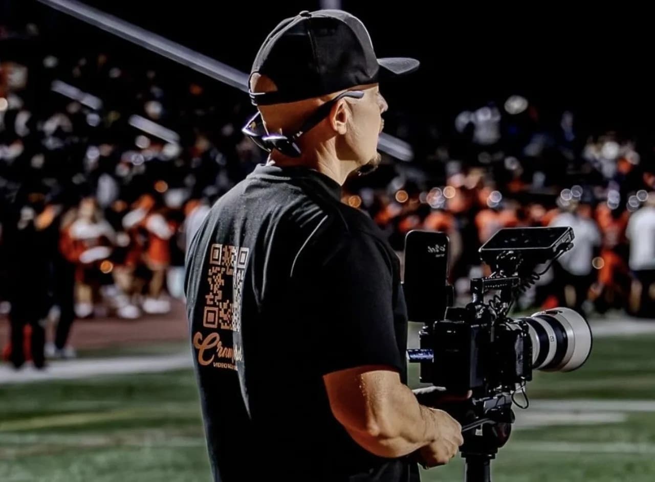 A Crawford Video videographer filming a youth football game from the sideline at night